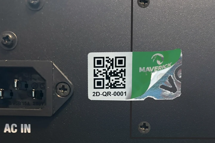 A partially peeled asset tag with a QR code and identification details affixed to electronic equipment.