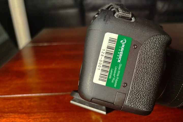 A close-up of a green custom asset tag with a barcode and identification details attached to a black device on a wooden surface.