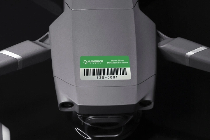 A green asset ID tag with a barcode and identification details affixed to a gray device on a black background.